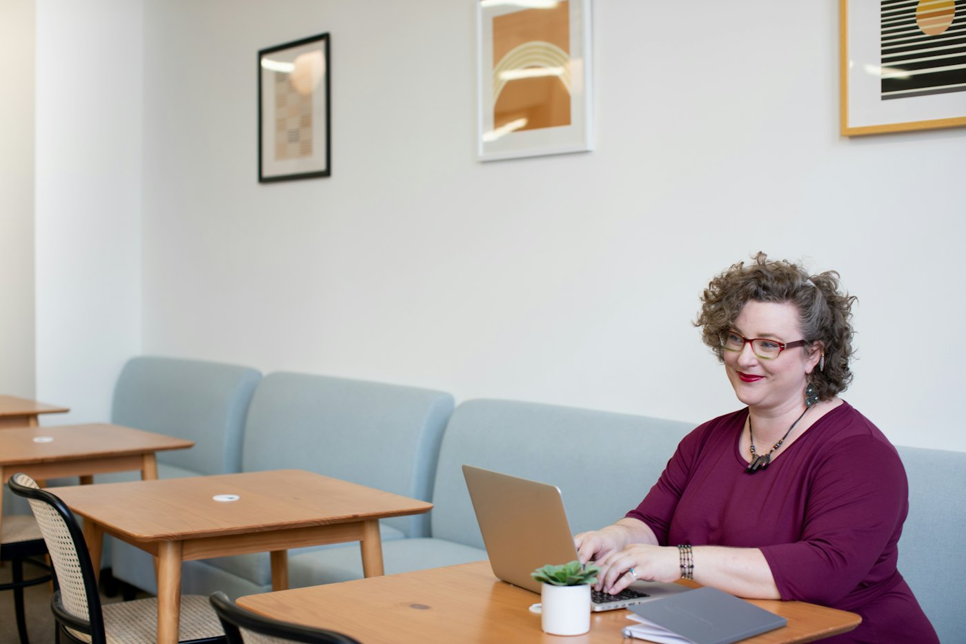 A woman in her fifties smiling at her laptop at a table